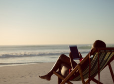 Rear view of woman using digital tablet while relaxing in a beach chair on the beach