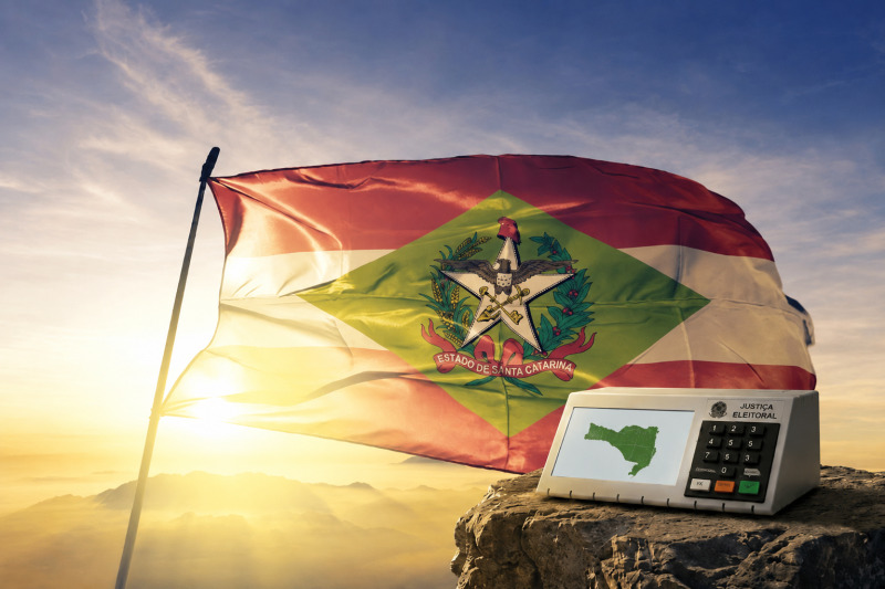 Bandeira de Santa Catarina e urna eletrônica com o mapa do estado